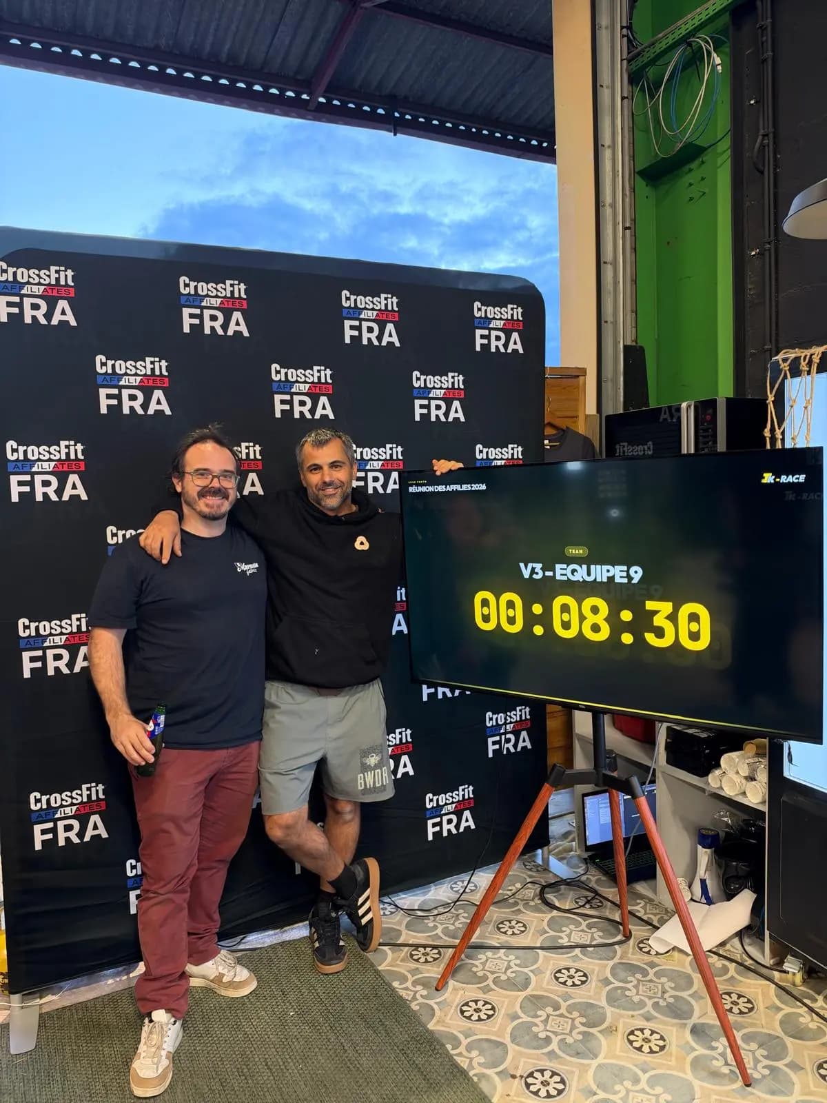 Two people next to the Tk-RACE finish board showing a team time at the 2026 affiliates meeting