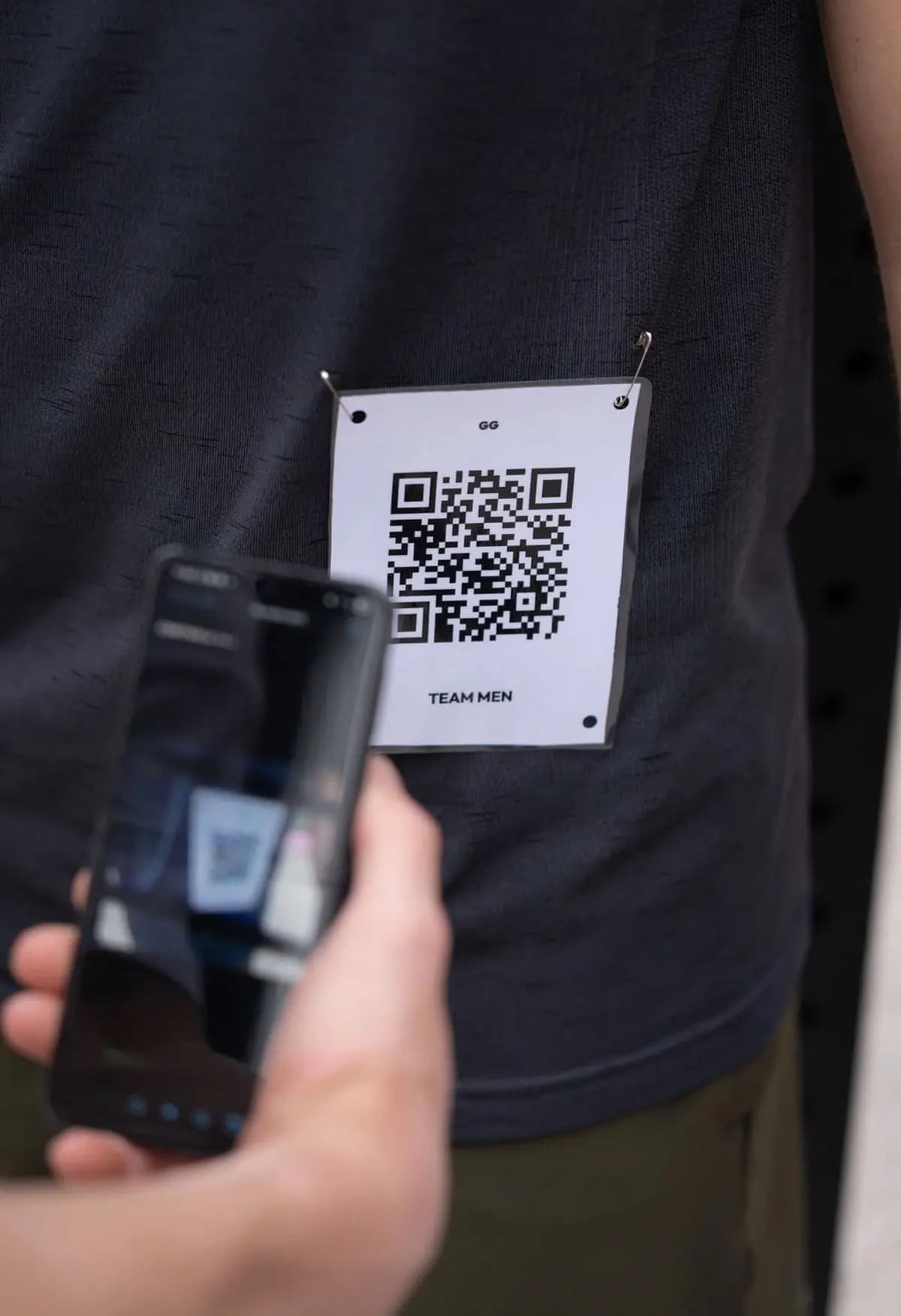 A volunteer's phone scanning the QR bib pinned to an athlete's shirt