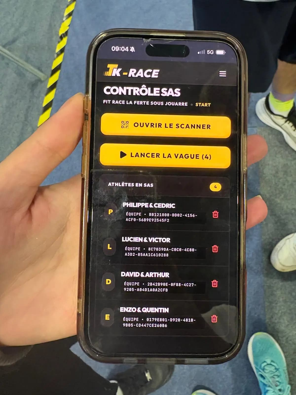 A volunteer's phone on the Tk-RACE start-pen screen, four teams checked in